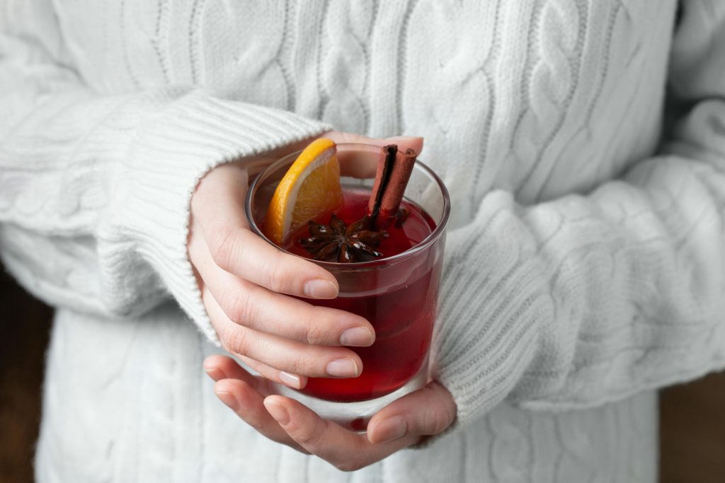A person in a jumper is holding a warm, festive cocktail.